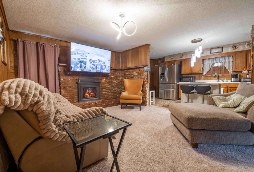 Open-concept living area featuring a brick fireplace, wood-panel accent walls, and carpet flooring