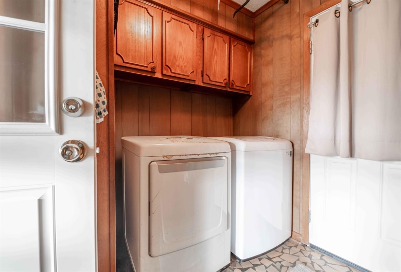 Dedicated laundry area featuring overhead cabinetry, wood paneling, and a durable tile floor