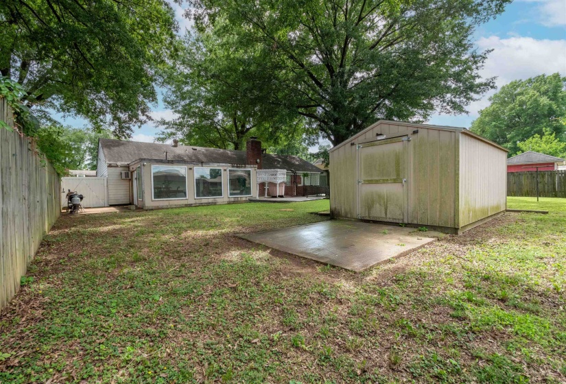 Expansive backyard featuring a detached storage shed, a concrete patio slab, and perimeter fencing