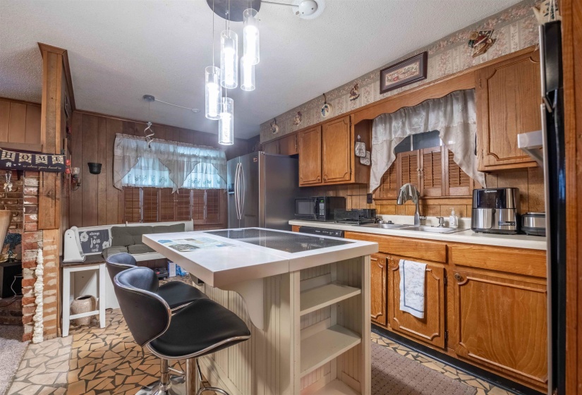Kitchen featuring wood-panel walls, wood cabinetry, a white countertop, and a built-in cooktop island with a contemporary pendant light fixture