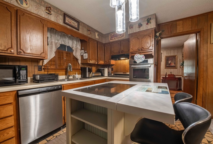 Kitchen featuring wood cabinetry, white countertops, built-in stainless steel appliances, and a central island with integrated cooktop