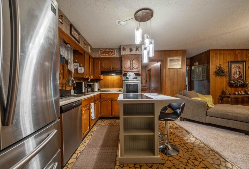 Kitchen featuring stainless steel appliances, wood cabinetry, built-in oven, and central island with cooktop and pendant lighting
