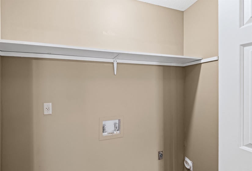 Laundry area featuring a built-in white shelf, warm neutral wall paint, white trim, and utility connections