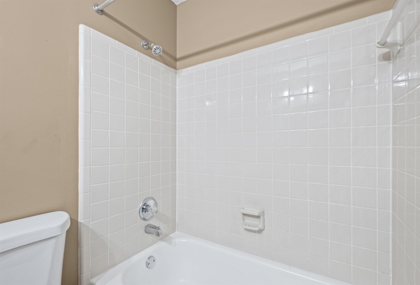 Bathtub with white square tile surround, chrome fixtures, and a shower head