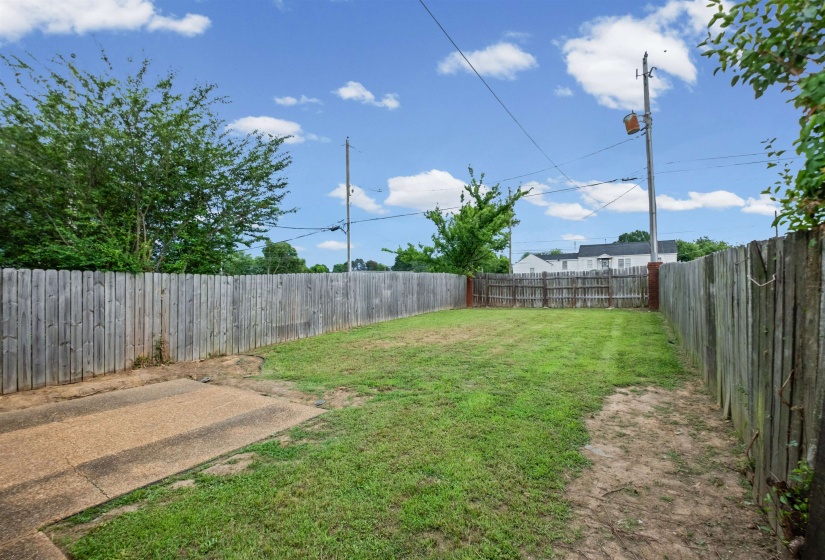 Expansive backyard featuring a manicured lawn, established privacy fencing, and a concrete patio area
