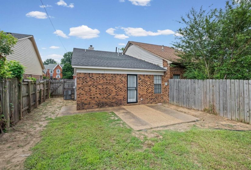 Rear exterior featuring brick siding, a security screen door, and a concrete patio