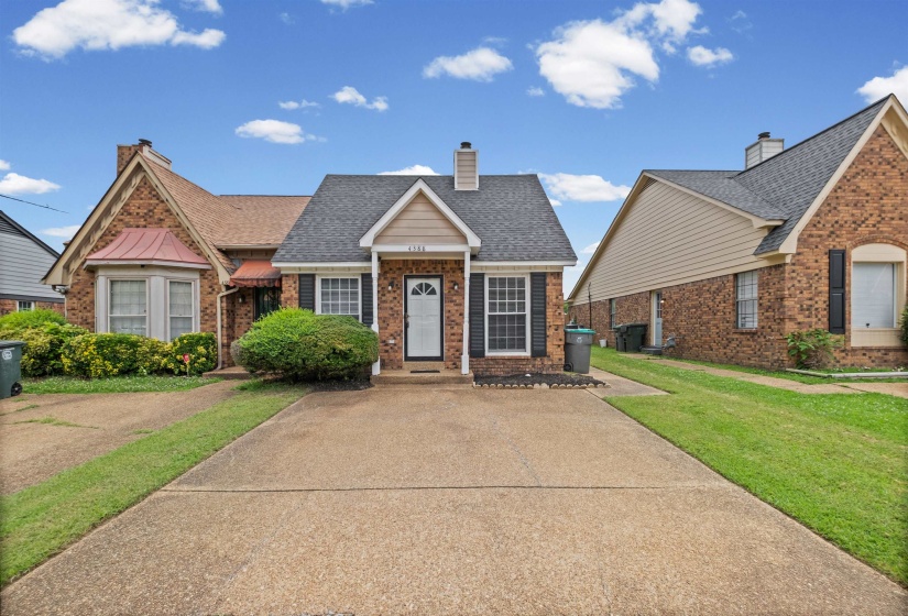 Brick exterior with a gabled roofline, decorative shutters, a front entry door with a storm door, and a concrete driveway