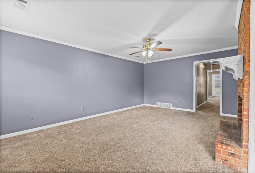 Spacious room featuring neutral carpet, a ceiling fan, crown molding, and a brick fireplace