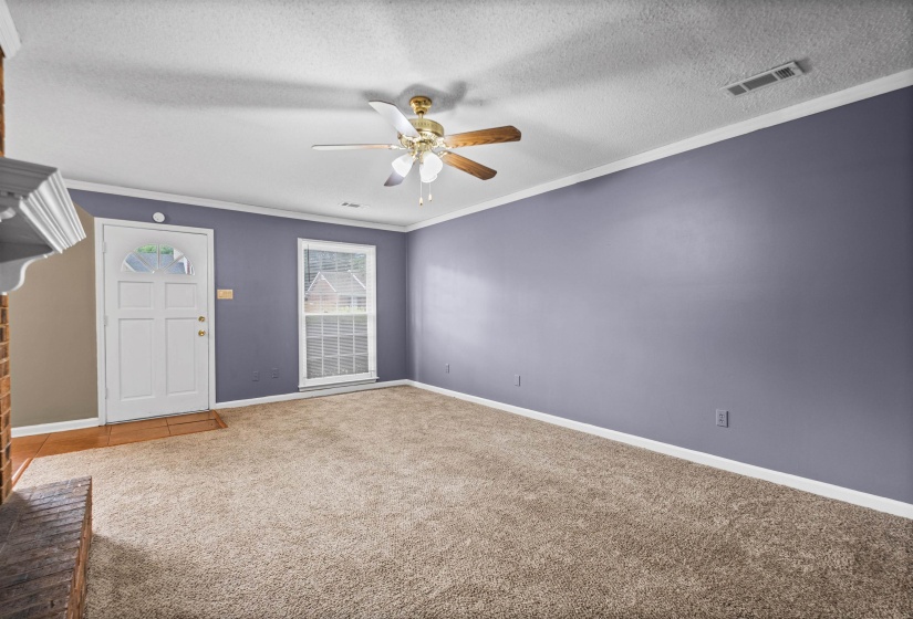 Living area featuring plush carpeting, a ceiling fan with integrated lighting, a multi-pane window, and a white entry door