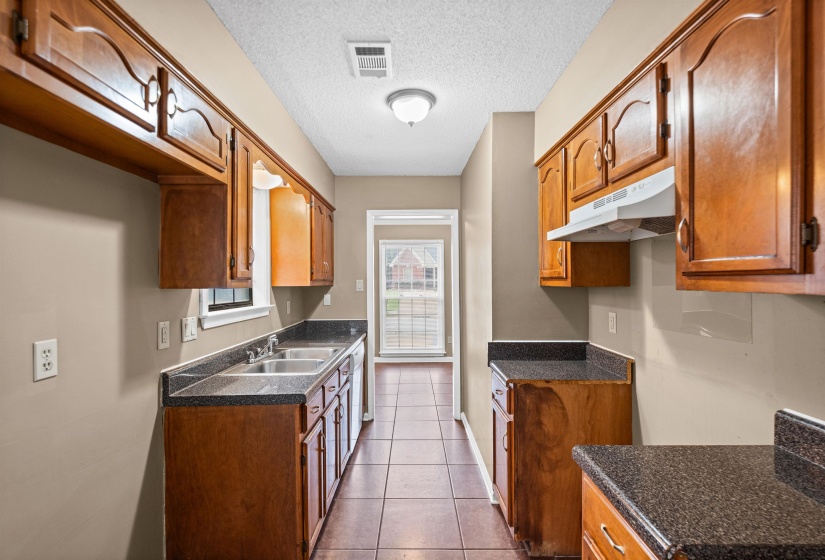 Galley kitchen featuring wood cabinetry, dark speckled countertops, a double basin sink, and tile flooring