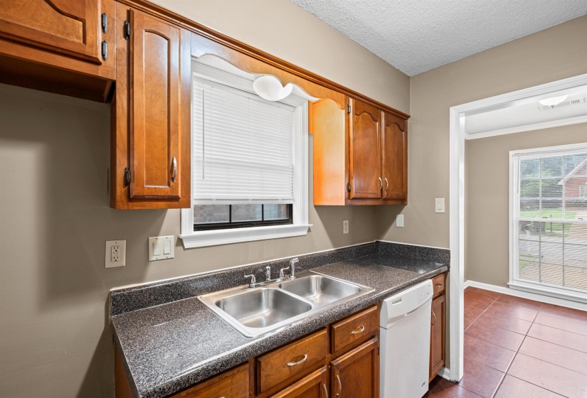 Kitchen featuring a double basin stainless steel sink, dark speckled countertop, wood-finish cabinetry, and a white dishwasher