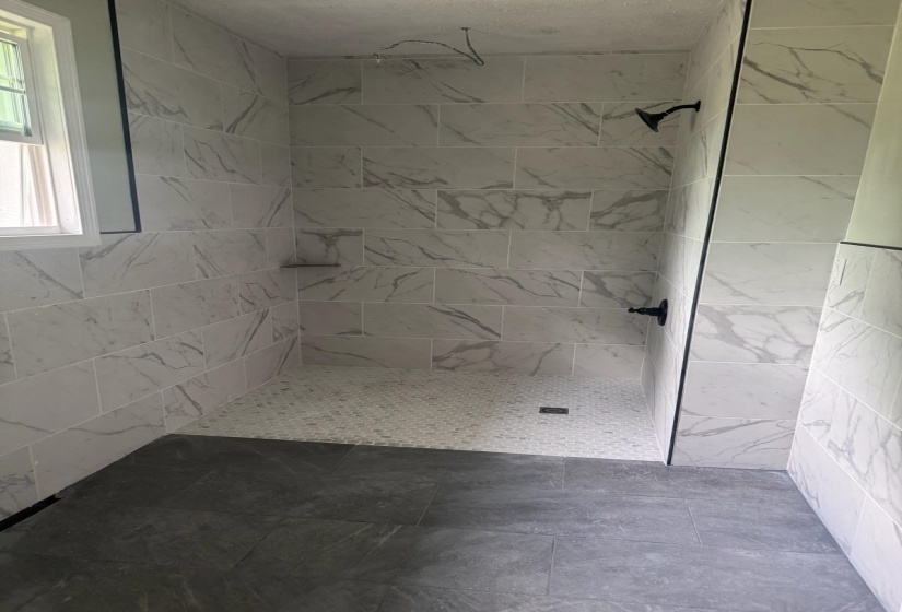 Walk-in shower featuring large format marble-look wall tiles, pebble-style floor tiling, a built-in shower niche, and matte black shower fixtures