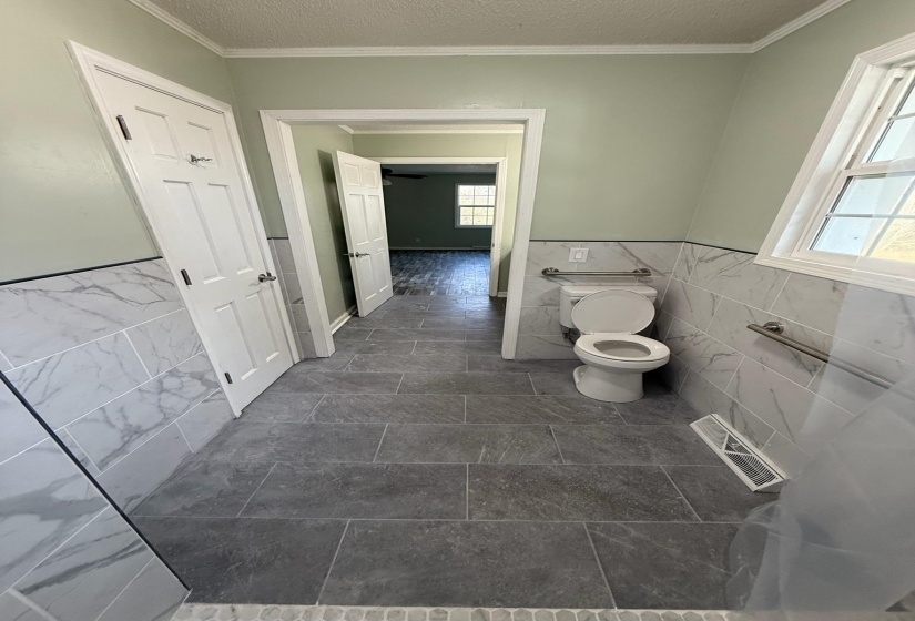 Bathroom featuring grey floor tiling, white marble-patterned wall tile wainscoting, and light green walls
