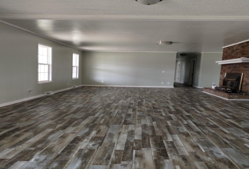 Spacious room featuring wood-finish flooring, a brick fireplace with a white mantel, light-toned walls, multiple windows, and white trim throughout