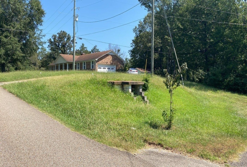 Brick exterior home featuring an attached garage, covered front porch, and a sloped, expansive front yard