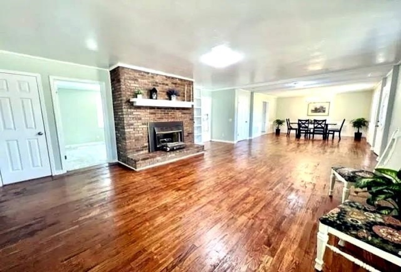 Spacious interior featuring wood-finish flooring, a brick fireplace with a white mantel, and built-in shelving