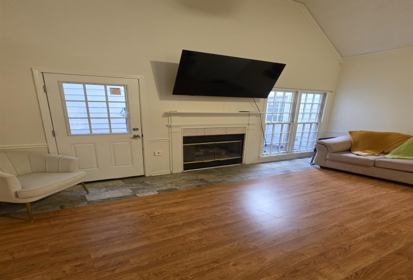 Vaulted ceiling room featuring a fireplace with a white mantel, glass-paneled exterior door, and large window