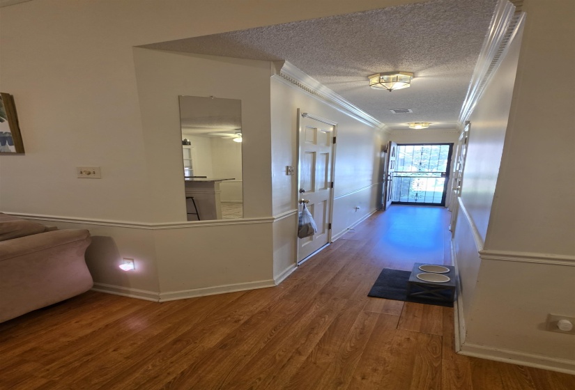 Hallway featuring wood-finish flooring, crown molding, and wainscoting details