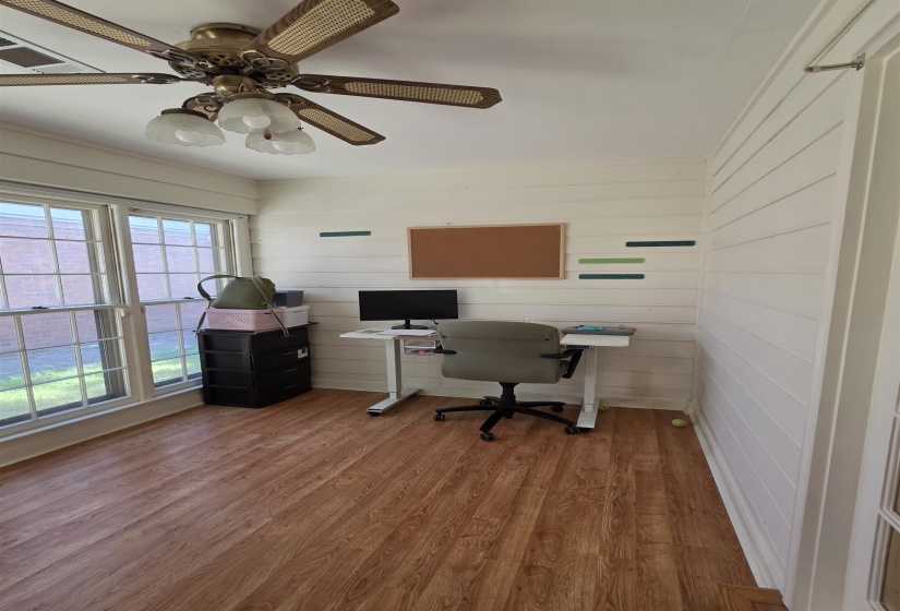 Room featuring wood-finish flooring, white shiplap walls, a ceiling fan with integrated lighting, and multiple windows