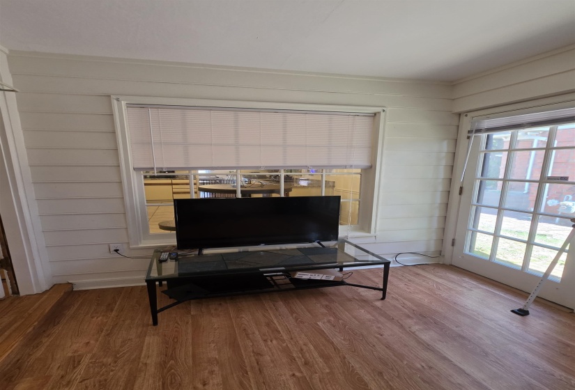 Interior space featuring wood-finish flooring, horizontal paneling on walls, a large window with horizontal blinds, and a glass-paneled exterior door