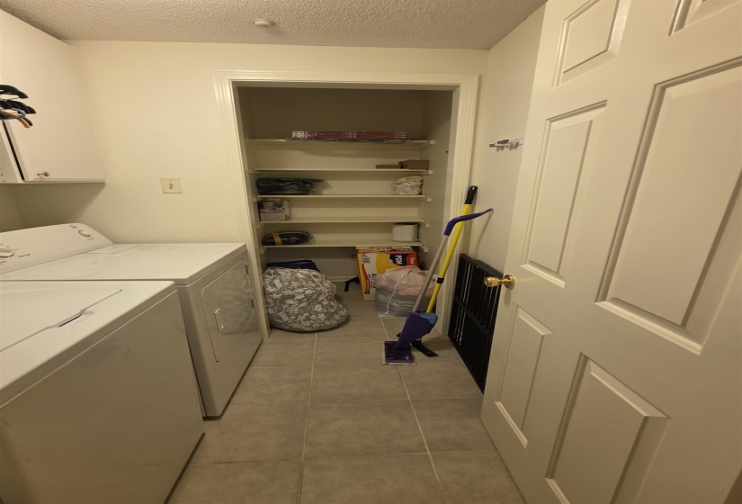 Laundry area featuring light-toned tile flooring, built-in shelving, and a solid interior door