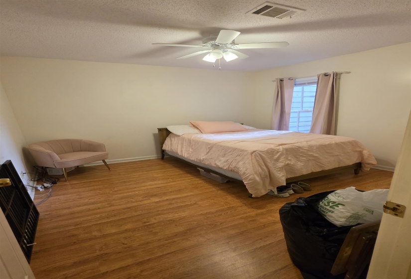 Room featuring wood-finish flooring, a ceiling fan with integrated lighting, and a window with curtain rods
