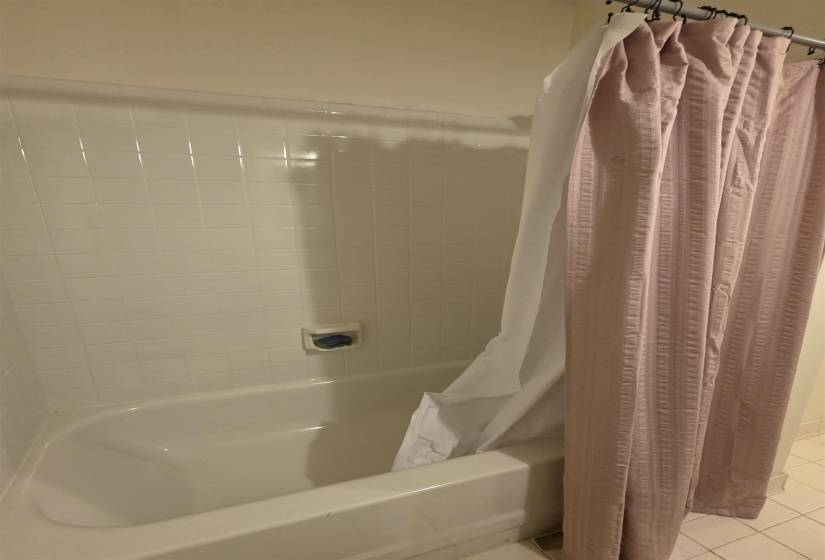White ceramic tile surrounds a drop-in bathtub with integrated soap dish