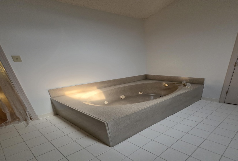 Built-in jetted tub with integrated surround, chrome fixtures, and white tiled flooring