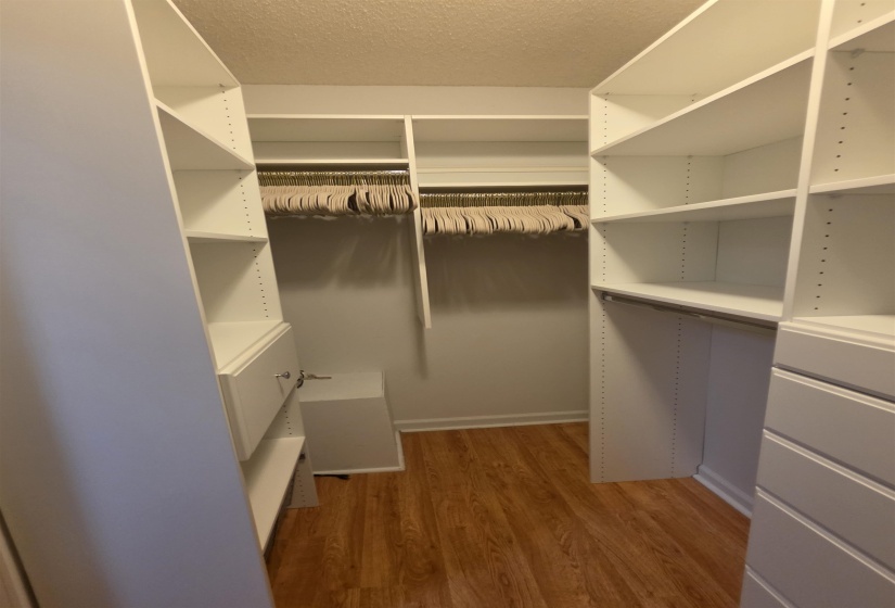 Custom closet system featuring white shelving and integrated drawers, multiple hanging rods, and wood-finish flooring