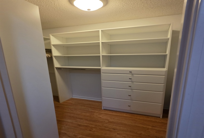White custom closet system featuring adjustable shelving, integrated drawer storage with silver hardware, and a hanging rod