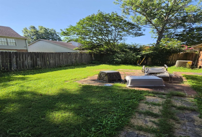 Private backyard featuring a wooden privacy fence, mature trees, and a brick patio area