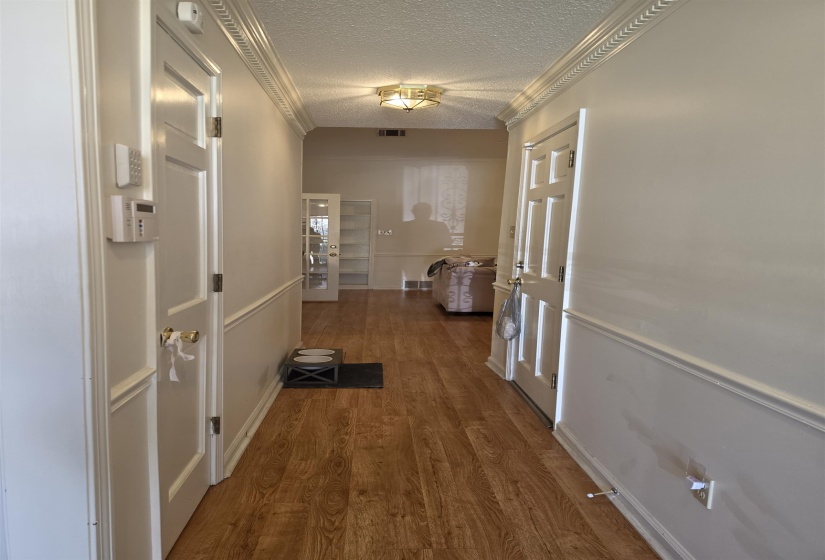 Hallway featuring wood-finish flooring, wainscoting, crown molding, and a flush-mount ceiling light fixture
