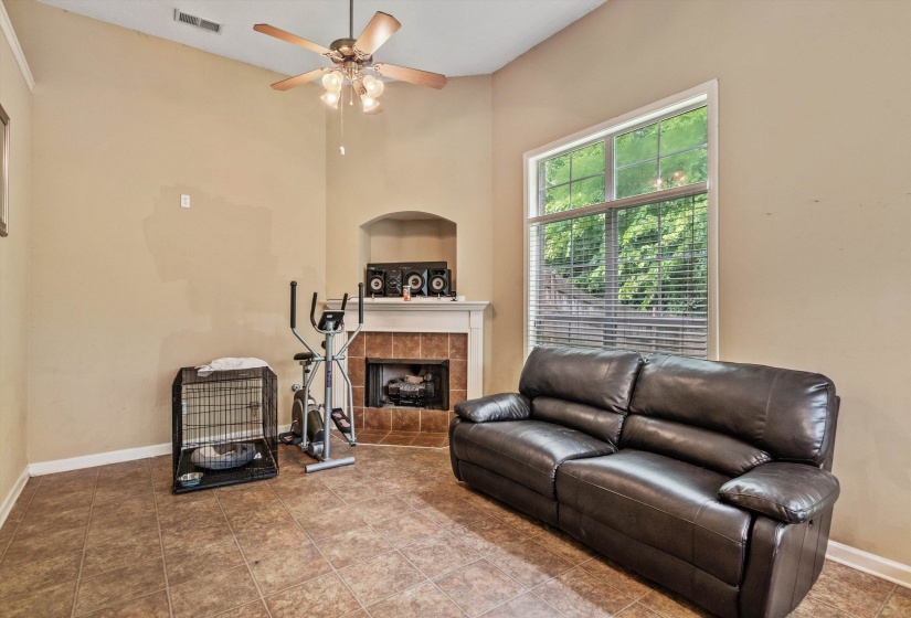 Vaulted ceiling with a ceiling fan, a tiled fireplace with a mantel, and a large window with blinds