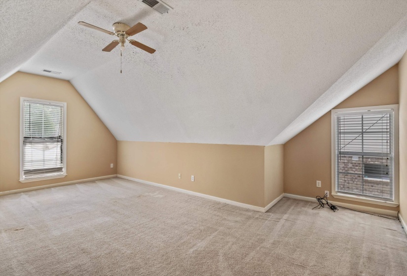 Expansive room featuring sloped ceilings, two windows with blinds, a ceiling fan, and light-toned carpeting