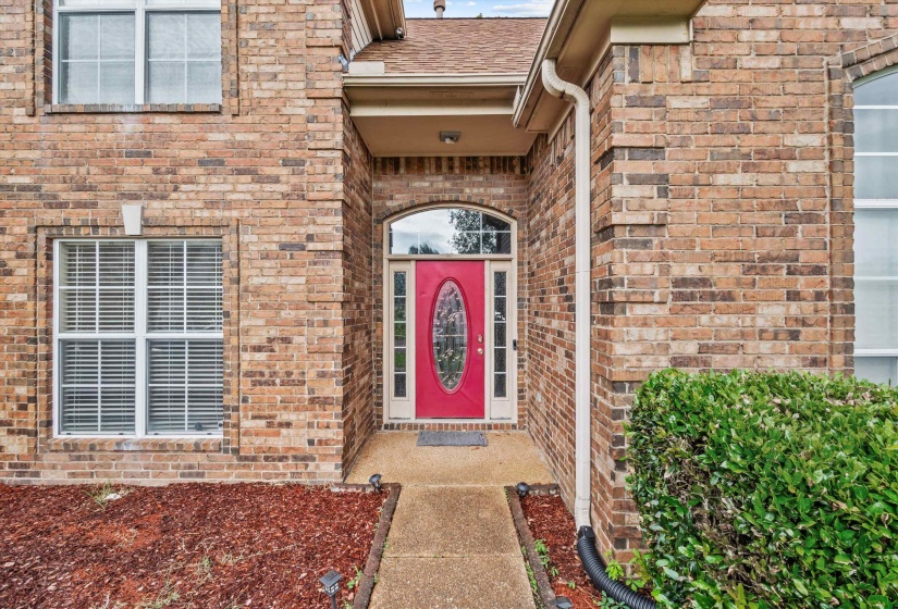 Brick exterior featuring a red entry door with an arched transom, a covered entry, and white-framed windows