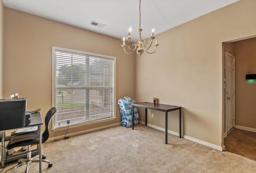 Versatile interior space featuring neutral wall tones, plush carpet flooring, a large window with blinds, and a brass chandelier fixture