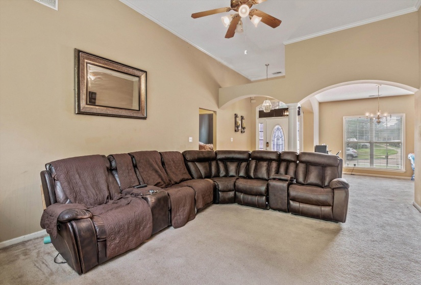 Spacious living area featuring vaulted ceilings, a ceiling fan, arched doorways, and light-colored carpet