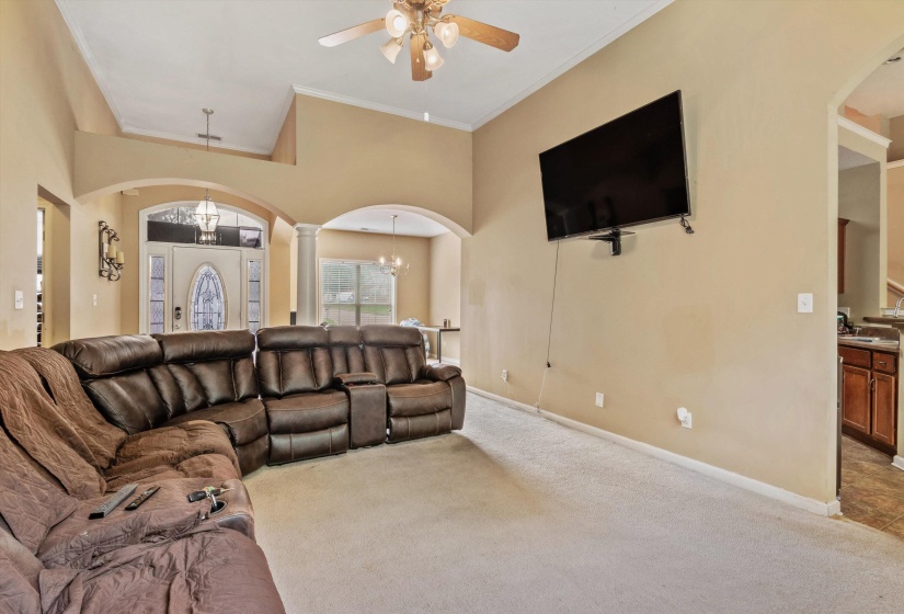 Carpeted living space featuring vaulted ceilings, arched doorways, a ceiling fan with integrated lighting, and a wall-mounted television bracket