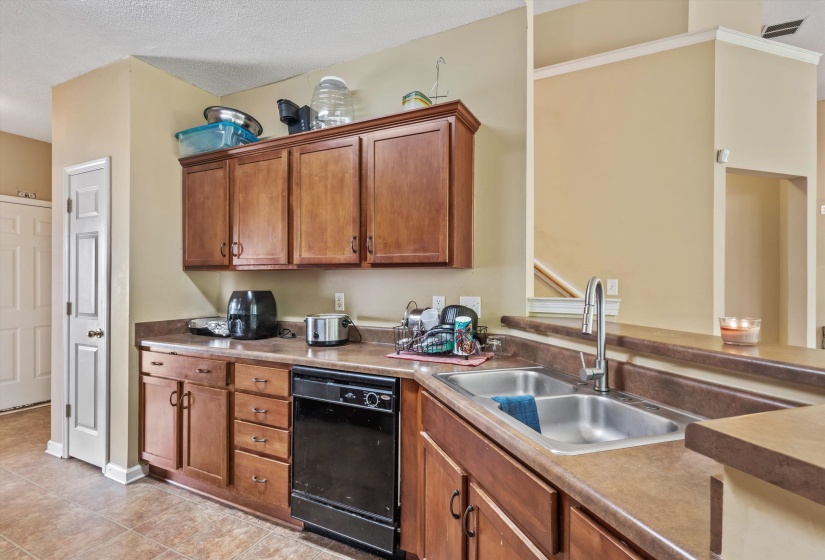 Kitchen featuring wood-finish cabinetry, a double basin stainless steel sink with a gooseneck faucet, black dishwasher, and a laminate countertop