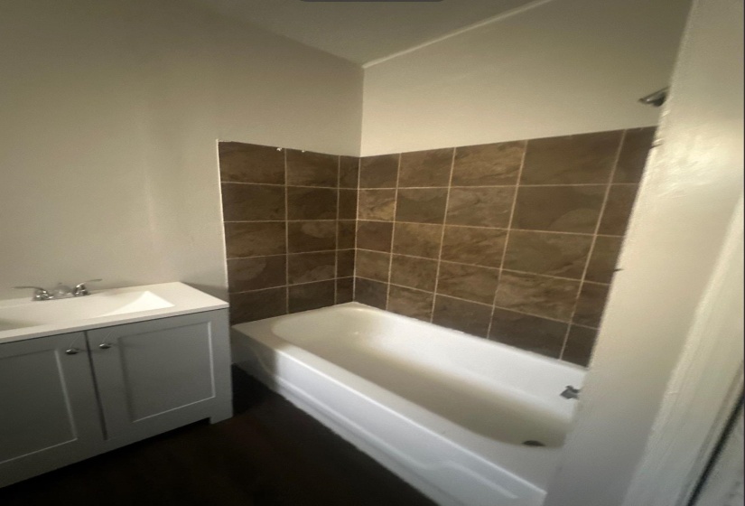 Full bathroom with a white tub-shower combination, brown wall tiling, and a gray vanity cabinet with an integrated sink