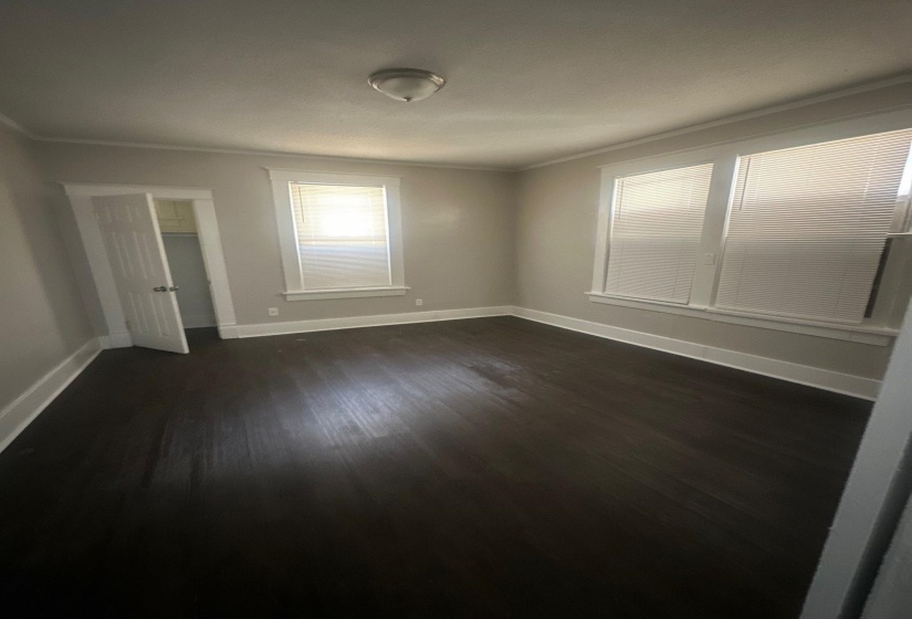 Room featuring dark wood-finish flooring, light grey painted walls, white trim, and multiple windows with blinds