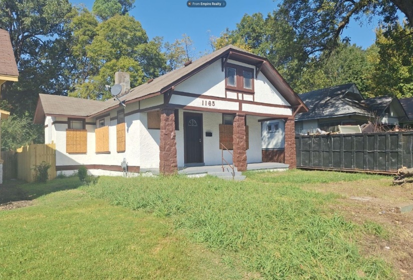 Gabled roofline with exposed eaves, exterior stucco finish, stone-clad porch columns, and a front entry door