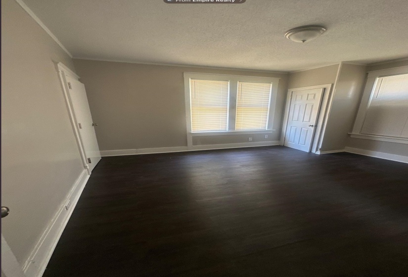 Room featuring dark wood-finish flooring, light-colored walls, white trim, and multiple windows with blinds