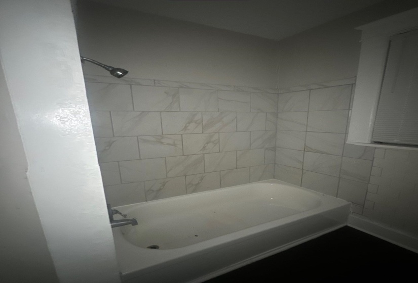 White bathtub with chrome fixtures, surrounded by white tile with grey veining
