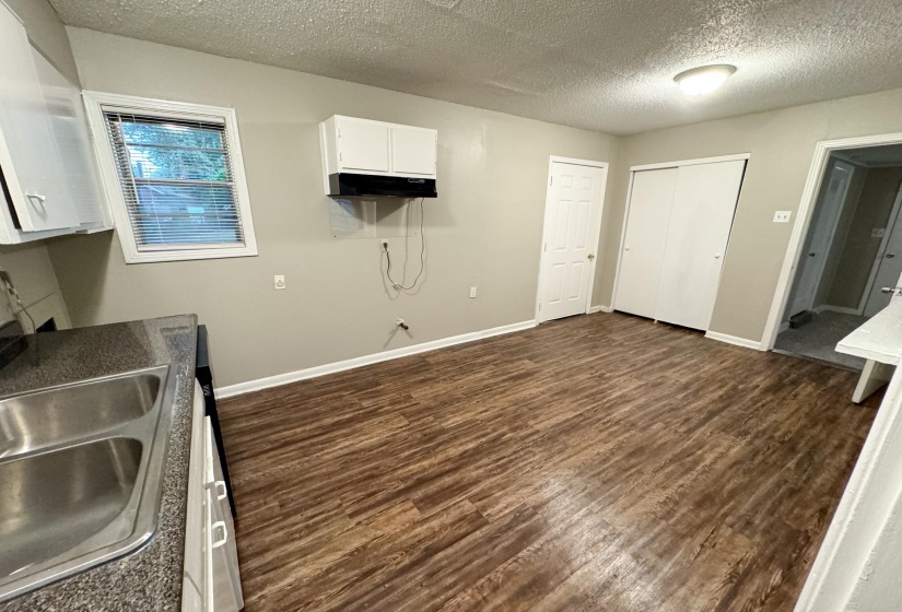 Spacious kitchen area featuring wood-finish flooring, white cabinetry, a double basin stainless steel sink, and a window with blinds
