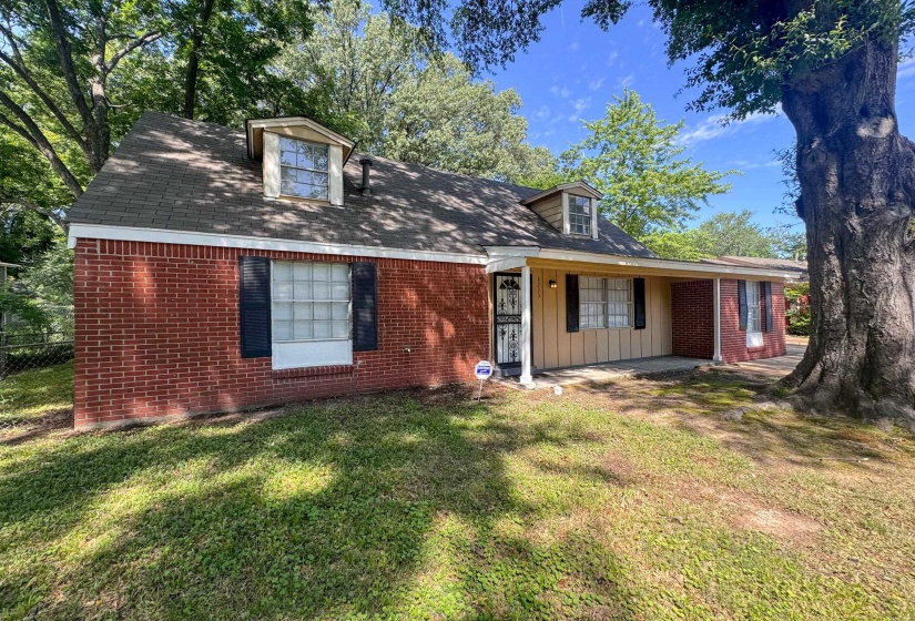 Brick exterior with a covered porch, dormer windows, and mature trees providing natural shade
