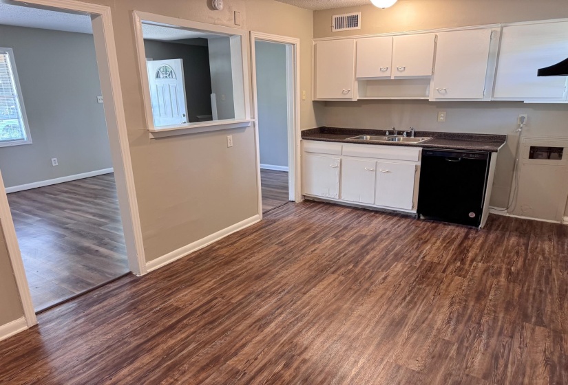 Kitchen space featuring wood-finish flooring, white cabinetry, a double basin sink, and a black dishwasher