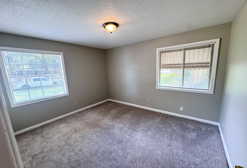 Carpeted interior space featuring two windows with white blinds, grey painted walls, and white baseboards