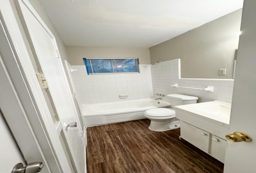 Bathroom featuring wood-finish flooring and a white tile surround bathtub with shower