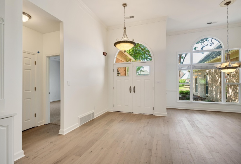 Vaulted entryway featuring double-door entry with arched transom, abundant natural light from large windows, wood-finish flooring, and two decorative pendant light fixtures